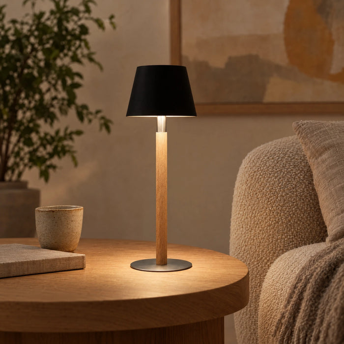 Nala rechargeable table lamp in solid oak with steel base and black shade, cordless on the dining table