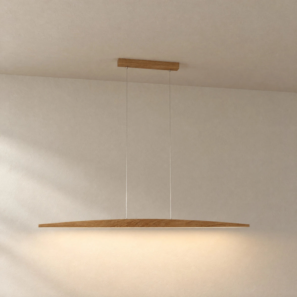 Elia oak pendant light against a light plaster wall: slim, curved wooden body on two stainless steel cables with warm downlight