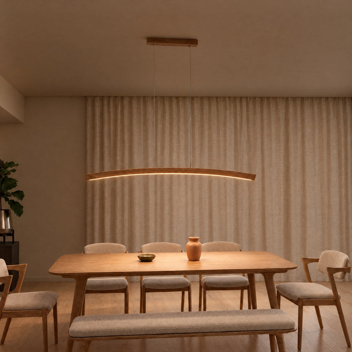 SpeicherArt Novara pendant light: curved solid oak arc, switched on above a wooden dining table in front of a light linen curtain