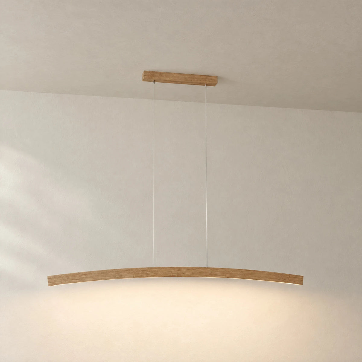 Novara oak pendant light against a light plaster wall: curved wooden arc on two stainless steel cables with warm downlight